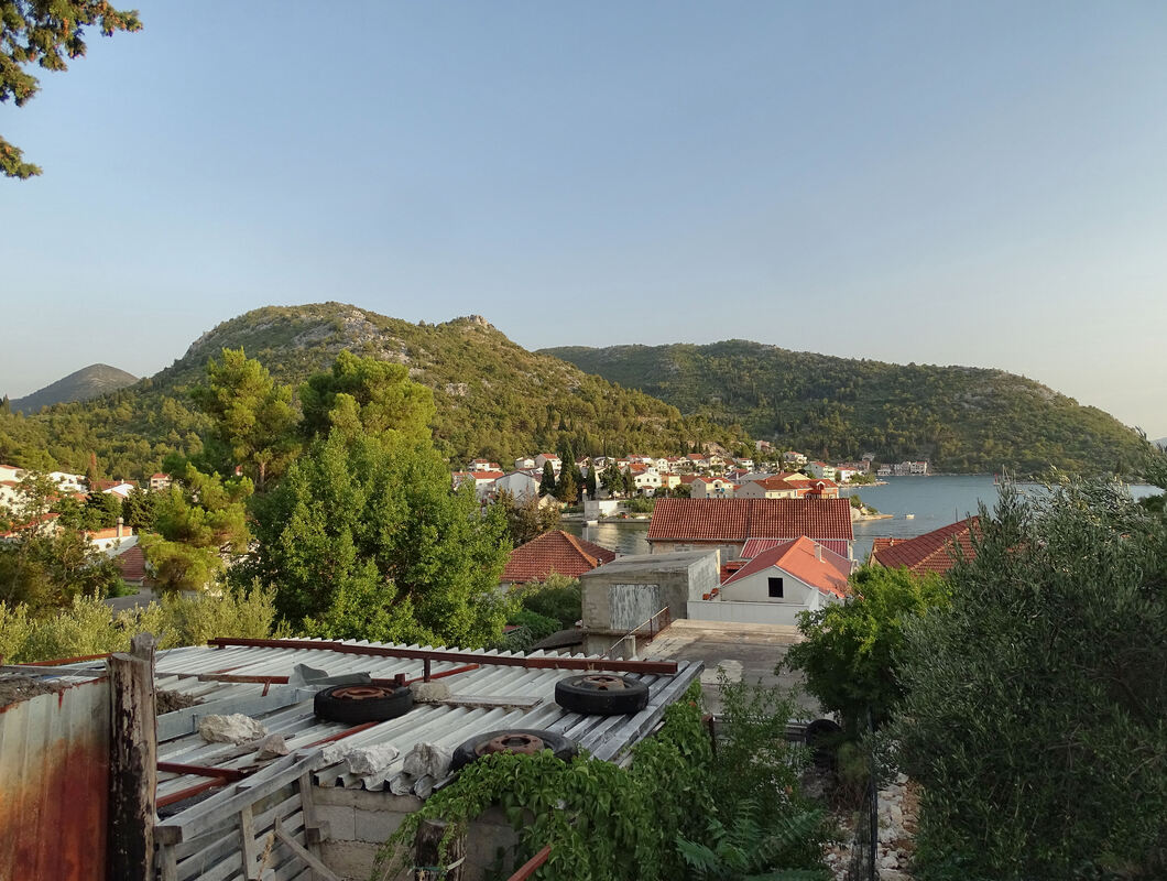 Pogled na selo Blace u slikovitom razvedenom zaljevu podno brda Planike (123 m) i desno pozadi vidi se par kuća naselja Dračeva Luka podno brda Orlić (270 m).